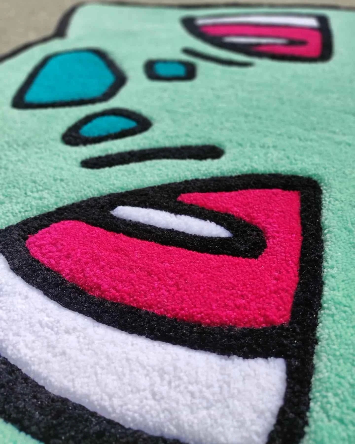 Turquoise Bulbasaur rug close-up with textured pink, white, and black shapes