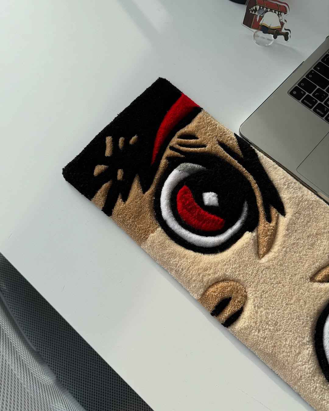 Handmade anime tufted desk mat corner with close-up red eye and black markings on tan