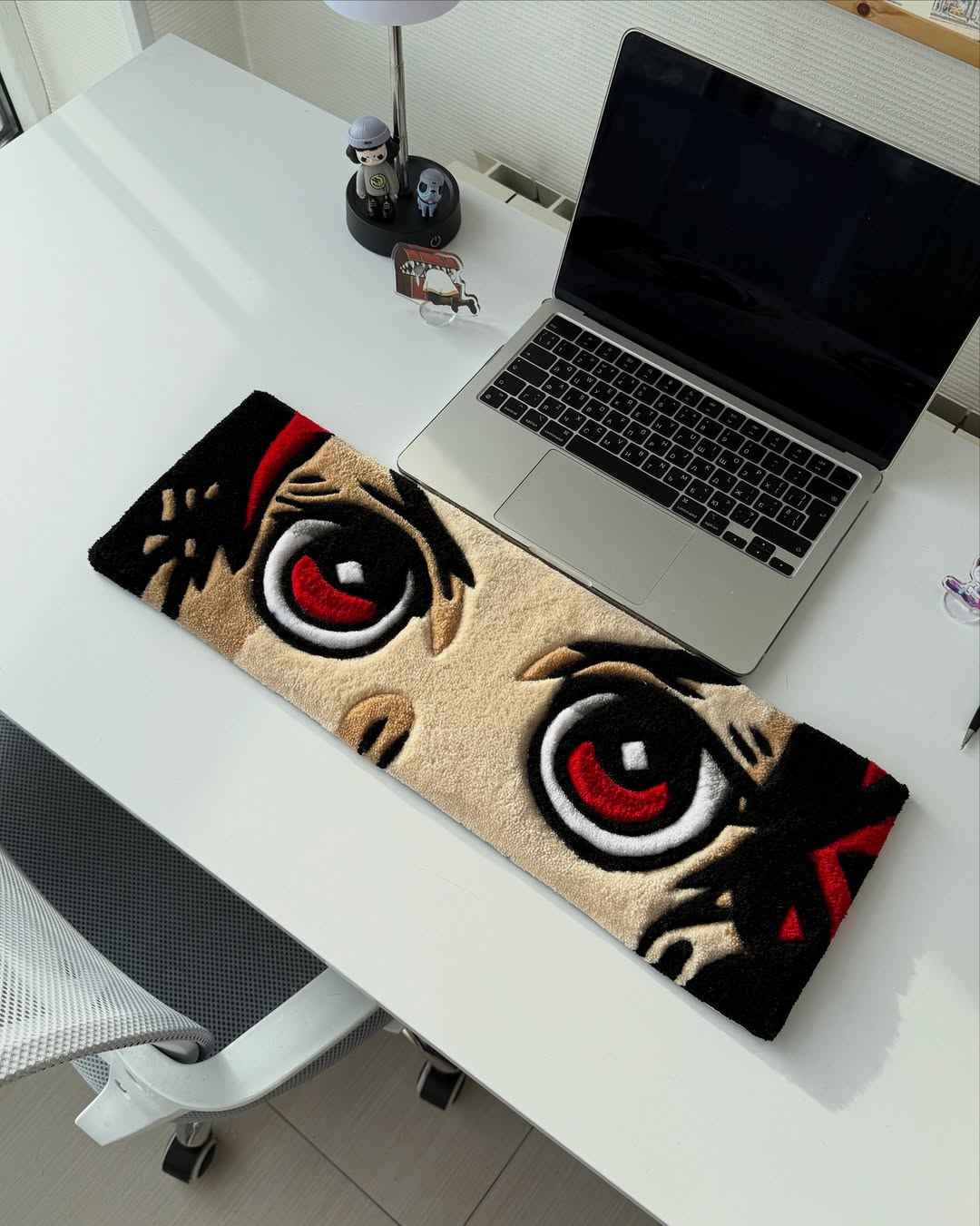 Handmade anime tufted desk mat laid on desk with two large red eyes and black details