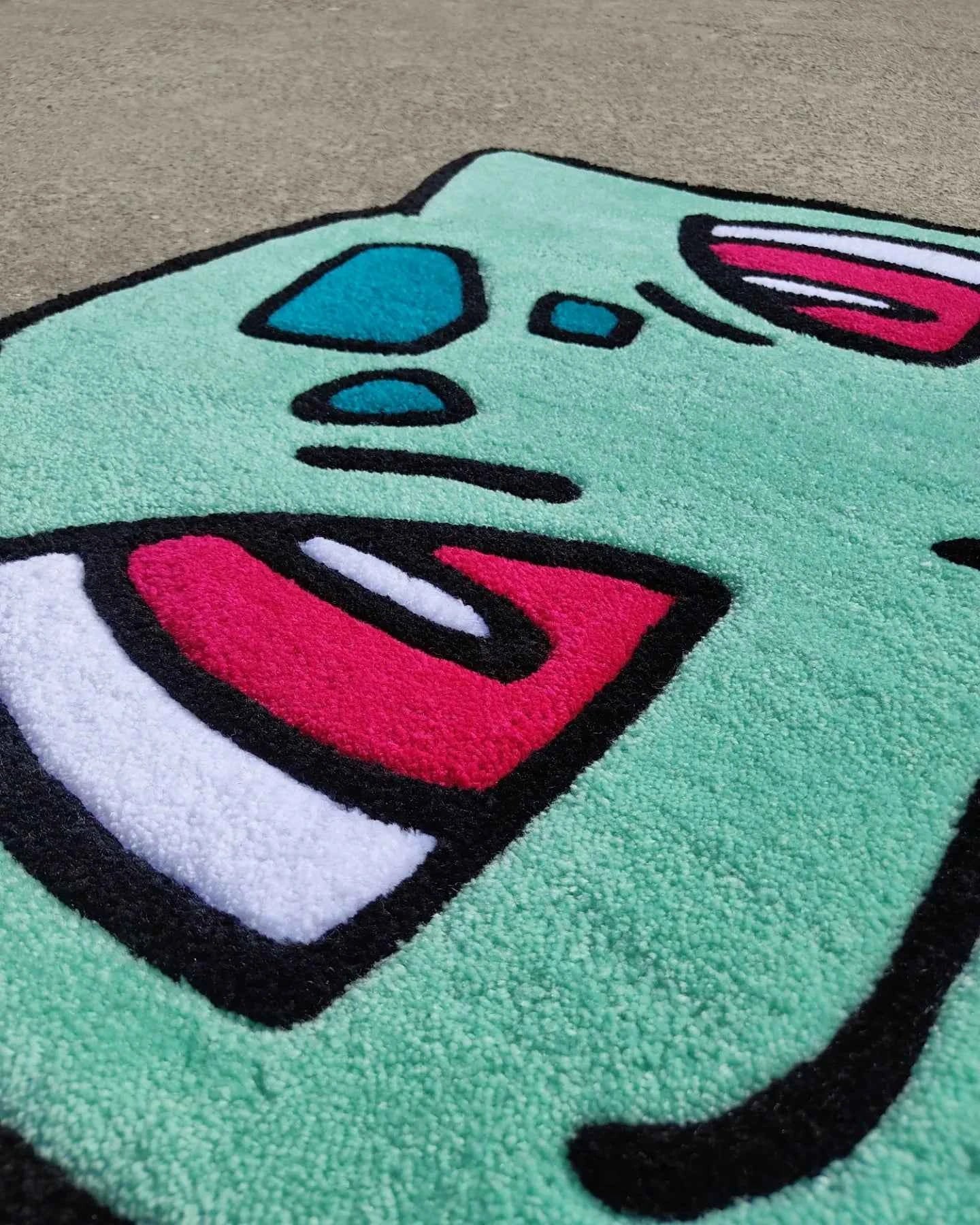 Turquoise Bulbasaur rug corner view with large pink-and-white eye and mouth patch